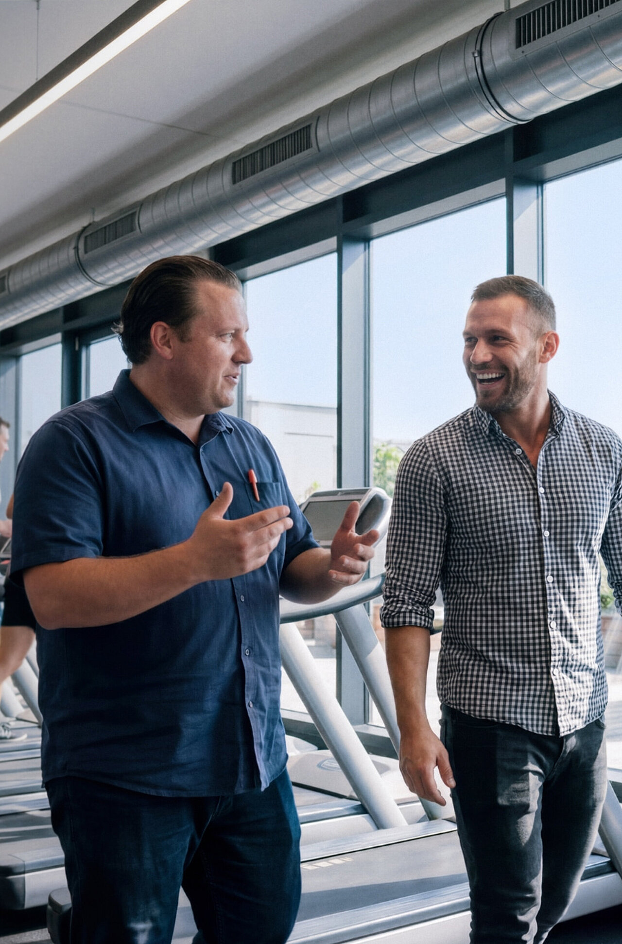 Two men—deep in conversation—walk past a row of treadmills set up in front of a large window. Outside the window stands an SMA Storage M.